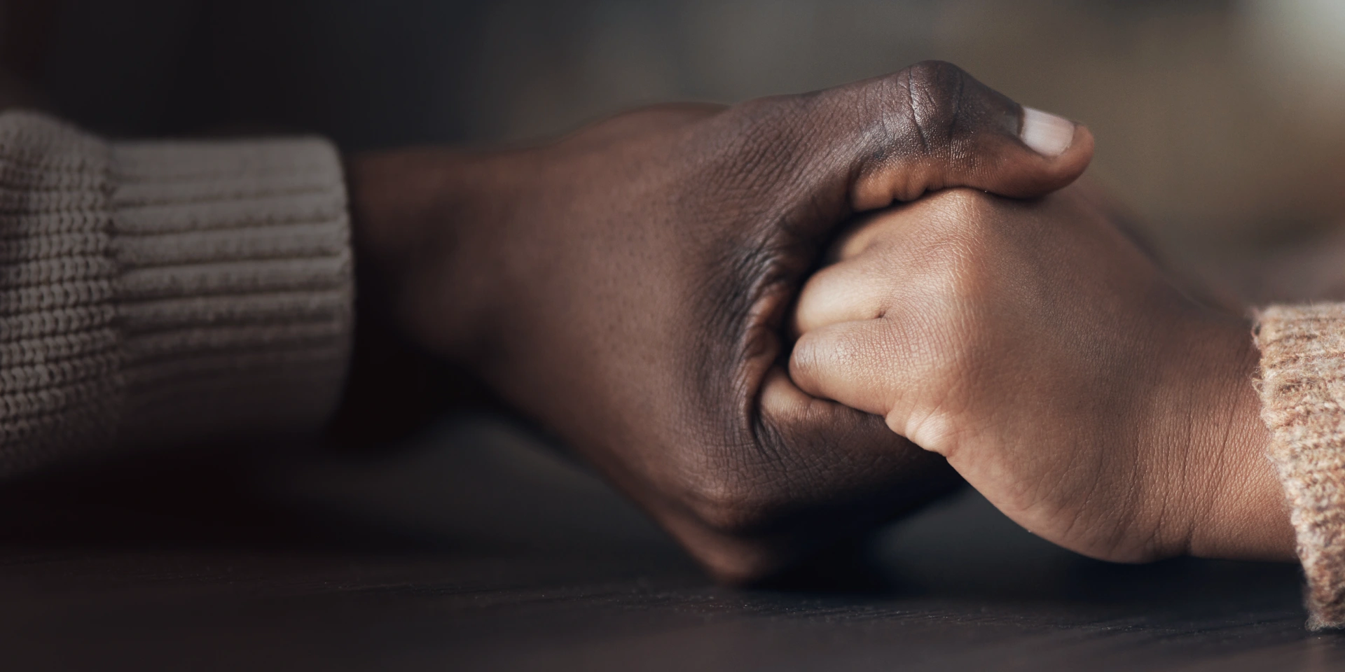 A close-up of two people holding hands, one with a darker skin tone and one with a lighter skin tone, both wearing sweaters.